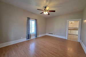 Spare room featuring light wood-type flooring, ceiling fan, hanging lights, and a textured ceiling