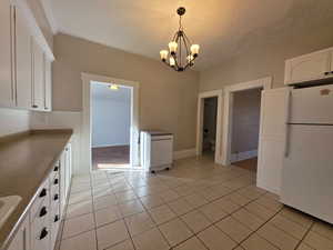 Kitchen with white cabinets, freestanding refrigerator, suspended lighting, light tile patterned floors, and a textured ceiling