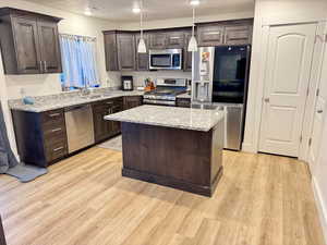 Kitchen with dark wood finish cabinetry, stainless steel appliances, a kitchen island, light wood finished floors, and light stone countertops