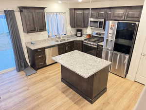 Kitchen featuring dark wood finish cabinets, stainless steel appliances, light stone countertops, and light wood-style floors