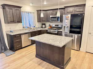 Kitchen with dark wood finish cabinets, stainless steel appliances, light stone counters, light wood-style flooring, and a kitchen island