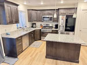 Kitchen featuring stainless steel appliances, dark wood finish cabinets, a kitchen island, light stone counters, and light wood finished floors