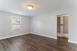 Empty room featuring a textured ceiling and dark wood-style flooring