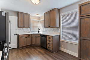 Kitchen with stainless steel appliances, light countertops, dark wood-type flooring, decorative backsplash, and wood finish cabinets