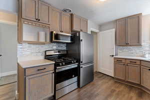 Kitchen featuring stainless steel appliances, light countertops, dark wood-type flooring, tasteful backsplash, and a textured ceiling