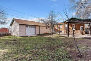 Rear view of property with an outdoor structure, a detached garage, a patio, and a pergola