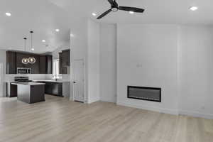 Kitchen featuring a kitchen island, light countertops, open floor plan, dark wood finish cabinets, and a glass covered fireplace