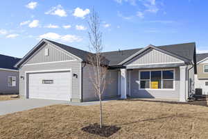 View of front facade featuring a front lawn, roof with shingles, concrete driveway, and board and batten siding