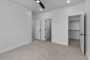 Unfurnished bedroom featuring a walk in closet, light carpet, recessed lighting, and ceiling fan