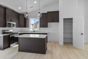 Kitchen with dark wood finish cabinets, stainless steel appliances, decorative backsplash, pendant lighting, and lofted ceiling