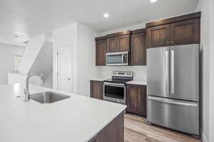 Kitchen featuring stainless steel appliances, dark wood finish cabinetry, light wood-style flooring, and light stone counters