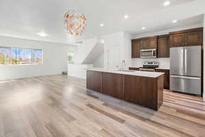 Kitchen featuring stainless steel appliances, dark wood finish cabinets, an island with sink, open floor plan, and light wood-style flooring