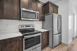 Kitchen featuring stainless steel appliances, dark wood finish cabinets, and light wood-style flooring