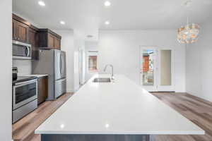 Kitchen with stainless steel appliances, dark wood finish cabinetry, light stone countertops, and light wood-style floors