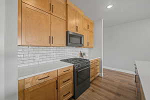 Kitchen featuring gas stove, black microwave, dark wood-style flooring, decorative backsplash, and light stone counters