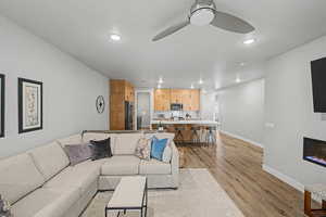 Living area with a ceiling fan, light wood-type flooring, recessed lighting, and a glass covered fireplace