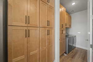 Laundry area featuring dark wood-style floors, washer and clothes dryer, cabinet space, and recessed lighting