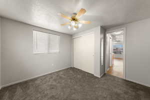 Unfurnished bedroom with dark colored carpet, a textured ceiling, a ceiling fan, and a closet