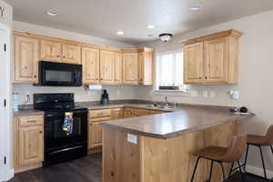 Kitchen featuring a peninsula, black appliances, light wood finish cabinets, recessed lighting, and a textured ceiling