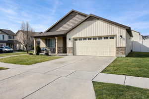 Craftsman-style house featuring stone siding, an attached garage, board and batten siding, and covered porch