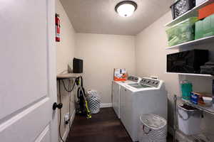 Laundry room with dark wood finished floors, a textured ceiling, and washing machine and clothes dryer