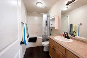Full bathroom featuring vanity, shower / bathtub combination with curtain, and dark wood-style flooring