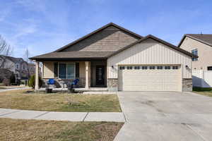 View of front facade with a porch, an attached garage, driveway, a front lawn, and stone siding