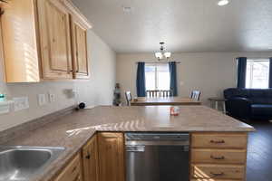 Kitchen with a peninsula, stainless steel dishwasher, open floor plan, light wood finish cabinets, and a textured ceiling