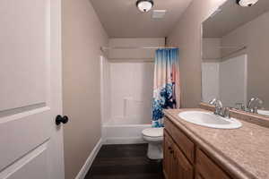 Full bath featuring vanity, shower / tub combo with curtain, and dark wood-style floors