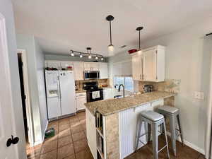 Kitchen featuring a kitchen breakfast bar, white cabinetry, white refrigerator with ice dispenser, and tasteful backsplash