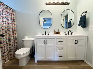 Full bath with double vanity, a shower with curtain, and light wood-style flooring