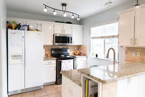 Kitchen with stainless steel appliances, a peninsula, light stone counters, backsplash, and rail lighting