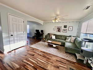 Living room with arched walkways, wood finished floors, ceiling fan, and ornamental molding