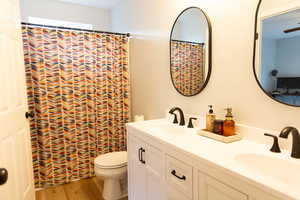 Bathroom featuring double vanity, a shower with shower curtain, and light wood-style flooring