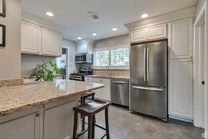Kitchen with stainless steel appliances, light stone countertops, recessed lighting, white cabinets, and a breakfast bar