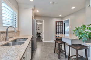 Kitchen featuring light stone counters, a breakfast bar, stainless steel appliances, recessed lighting, and white cabinetry