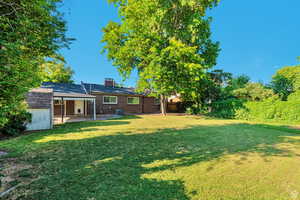 Rear view of property featuring brick siding, a patio, a chimney, a fenced backyard, and a shed