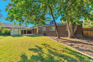Back of property featuring brick siding, a storage shed, a patio area, and a fenced backyard