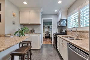 Kitchen featuring stainless steel appliances, recessed lighting, light stone countertops, a breakfast bar area, and white cabinetry