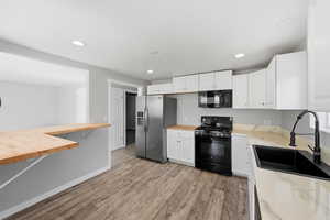 Kitchen with wooden counters, black appliances, white cabinets, light wood-style floors, and recessed lighting