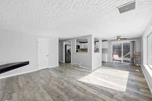 Unfurnished living room featuring light wood-type flooring, a ceiling fan, and a textured ceiling