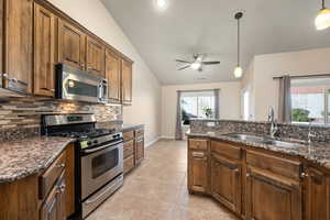 Kitchen with stainless steel appliances, dark stone counters, pendant lighting, ceiling fan, and lofted ceiling