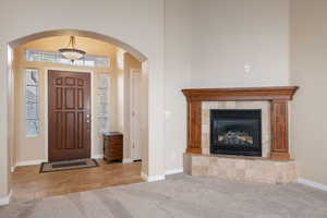 Foyer with arched walkways, light colored carpet, a fireplace, and light tile patterned floors
