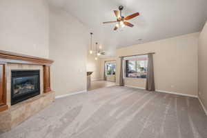 Unfurnished living room with a tiled fireplace, light carpet, ceiling fan, and lofted ceiling