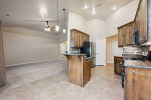 Kitchen with dark stone counters, decorative backsplash, stainless steel appliances, a breakfast bar area, and lofted ceiling
