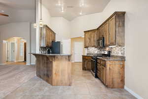 Kitchen featuring arched walkways, tasteful backsplash, dark stone countertops, light tile patterned flooring, and vaulted ceiling