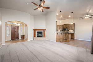 Unfurnished living room featuring ceiling fan, vaulted ceiling, light colored carpet, arched walkways, and a tile fireplace