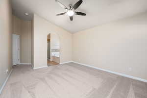 Master bedroom with a ceiling fan, light carpet, lofted ceiling, ensuite bath, and arched walkways
