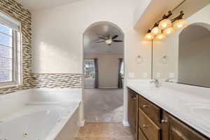 Full bathroom with double vanity, light tile patterned floors, light colored carpet, a jetted tub, and a ceiling fan