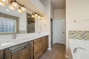Full bath featuring backsplash, double vanity, a garden tub, dark tile patterned floors, and a shower stall